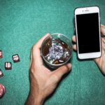 overhead-view-man-s-hand-holding-cellphone-whisky-glass-poker-table