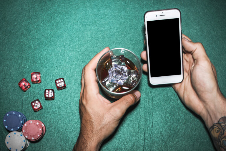overhead-view-man-s-hand-holding-cellphone-whisky-glass-poker-table
