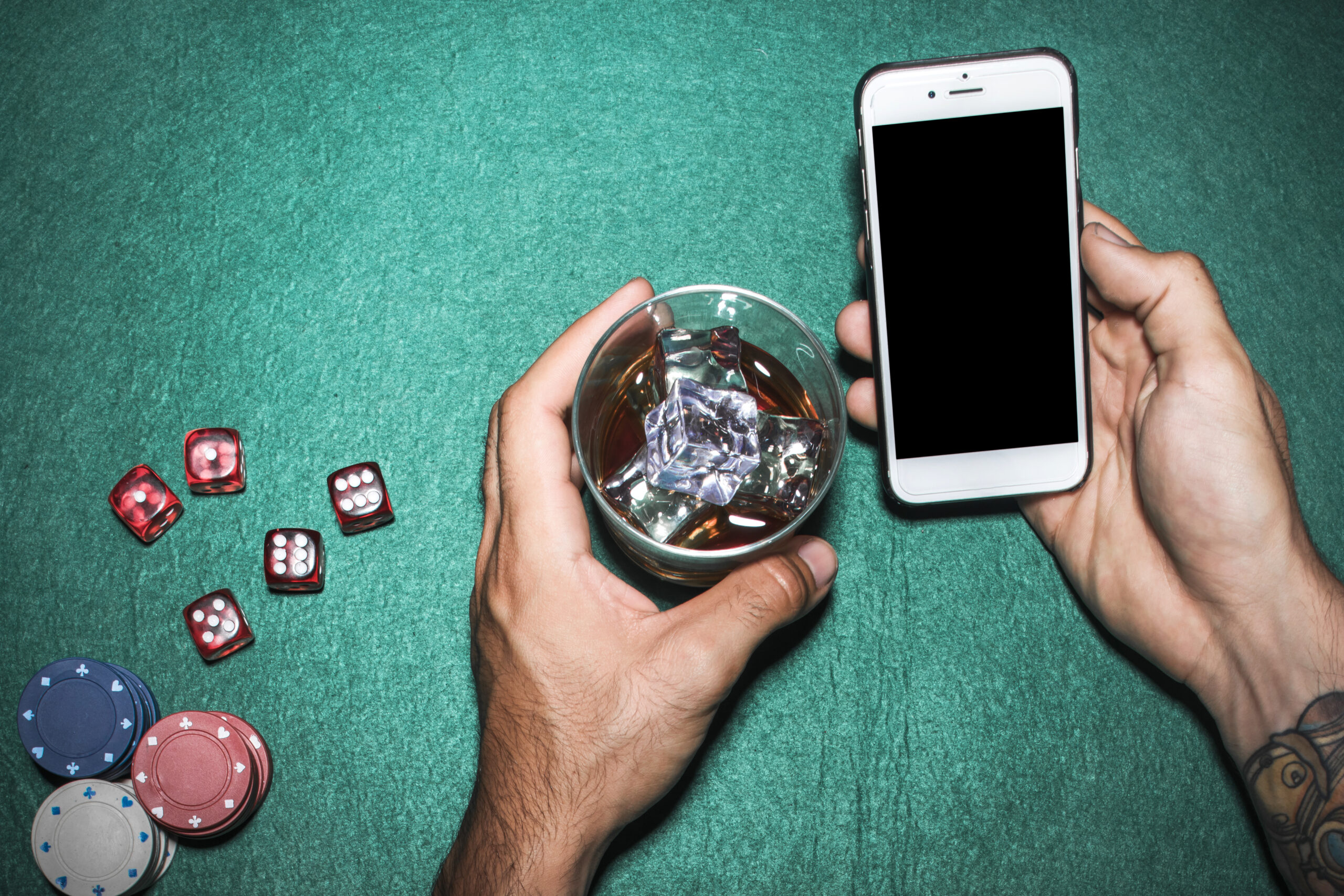 overhead-view-man-s-hand-holding-cellphone-whisky-glass-poker-table
